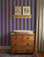 Brede Strepen Bordeaux Blauw – Atelier Chien : papier peint derrière une commode en bois avec panier à langer.